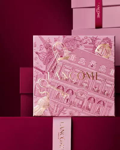 An elegant stack of pink and deep burgundy Lancome gift boxes, featuring a central box detailed with gold Parisian architectural illustrations.
