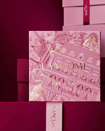An elegant stack of pink and deep burgundy Lancome gift boxes, featuring a central box detailed with gold Parisian architectural illustrations.