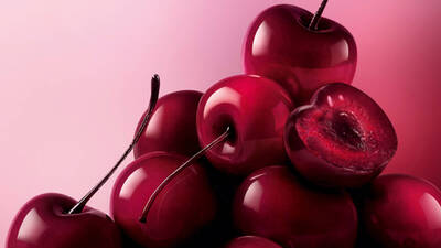 A pile of glossy, dark red to black cherries fills the bottom and right of the frame, set against a soft pink background.