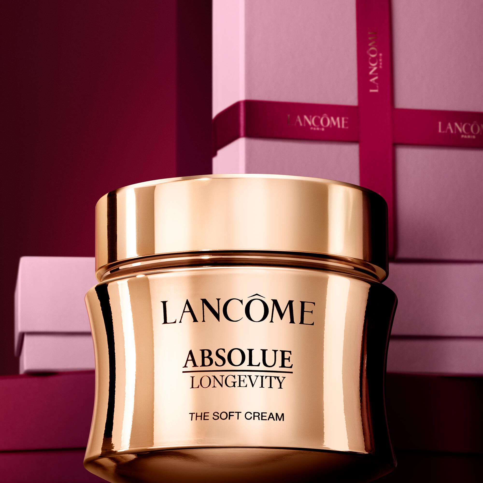 Image of Absolue Longevity Soft Cream standing in front of a pile of pink and dark red gift boxes, set against a dark red background.