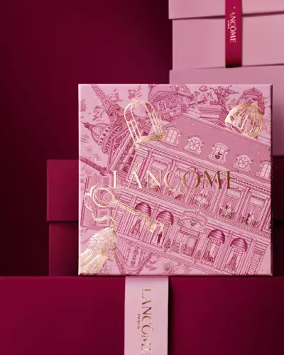 An elegant stack of pink and deep burgundy Lancome gift boxes, featuring a central box detailed with gold Parisian architectural illustrations.