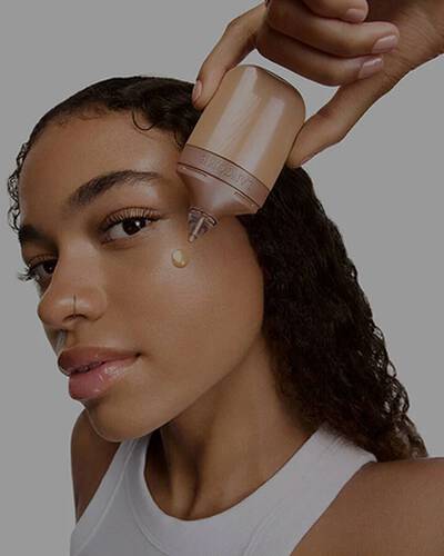 Model applying a drop of Lancome liquid highlighter to her cheek.