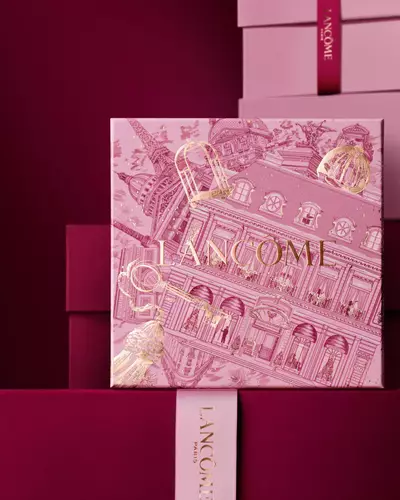Image of pink Lancome holiday gift box standing in front of a pile of pink and dark red gift boxes, set against a dark red background.