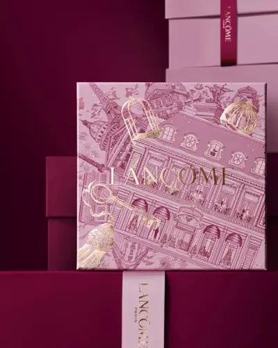 Image of pink Lancome holiday gift box standing in front of a pile of pink and dark red gift boxes, set against a dark red background.