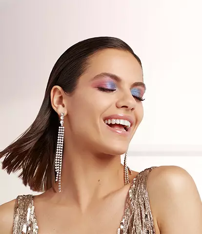 A smiling woman in a sparkling outfit with colorful makeup, showcasing a joyful expression.