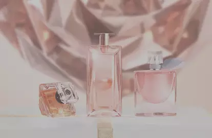 Three elegant perfume bottles are displayed on a white gift box decorated with a gold ribbon, against a shimmering, faceted background.