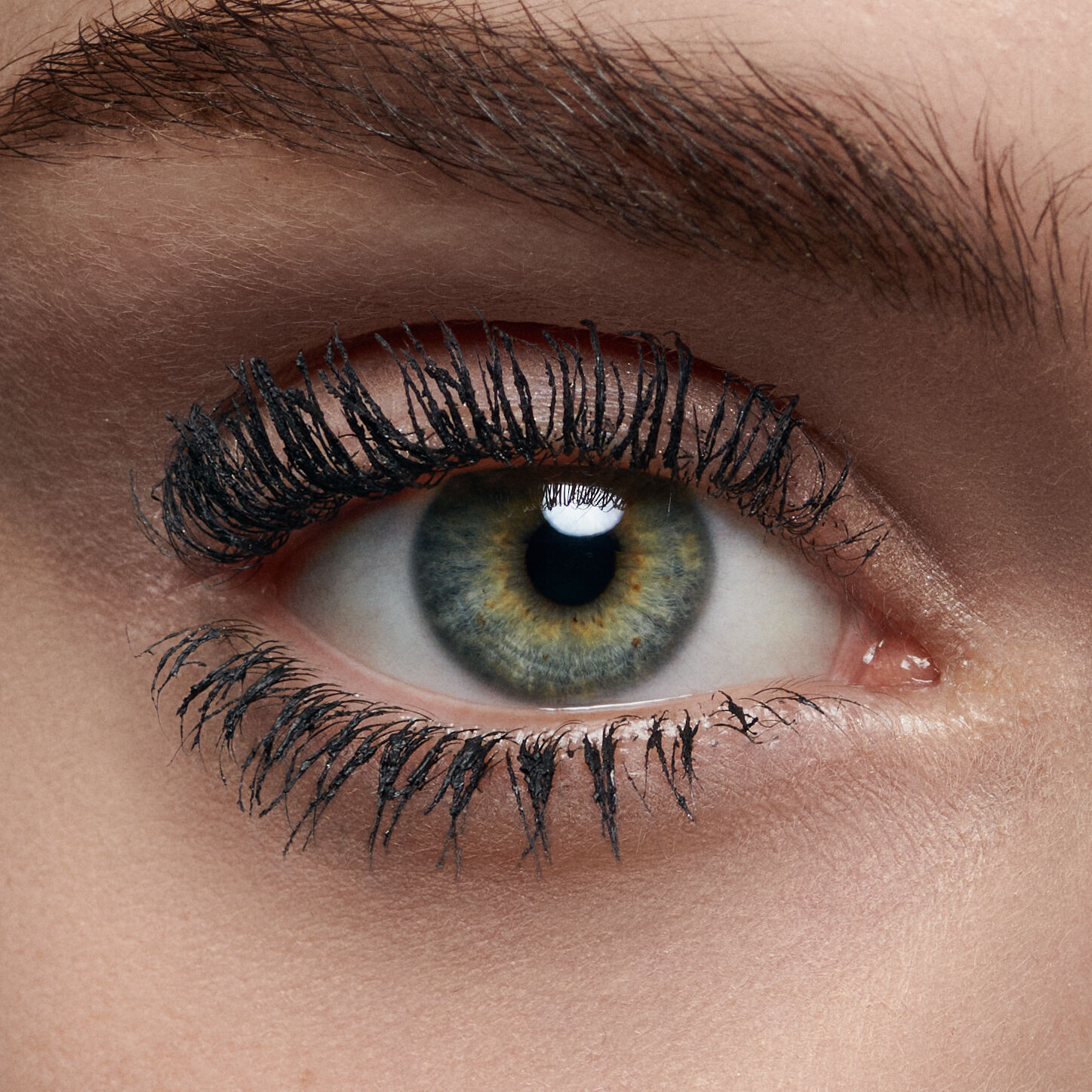Close-up of a human eye with striking green and brown hues, framed by long, dark eyelashes.