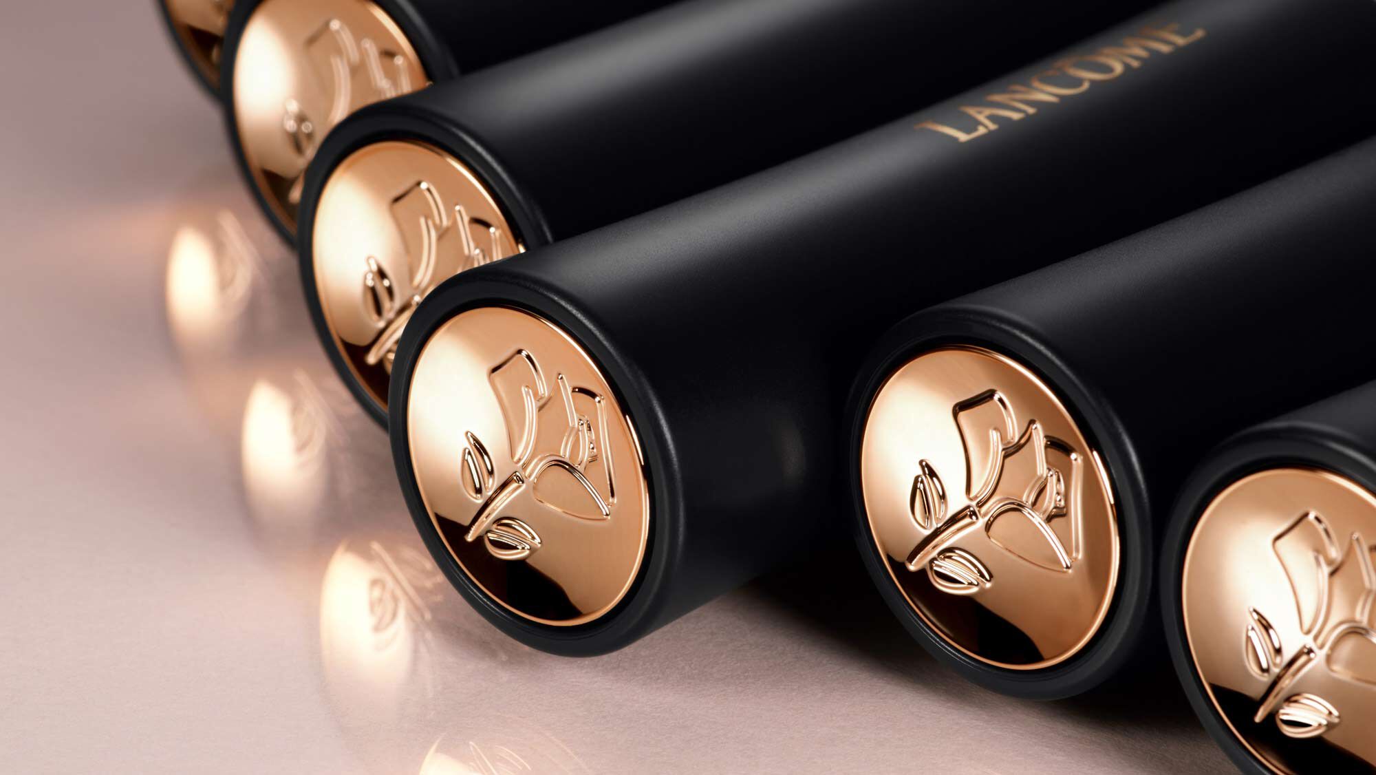 A close-up image of several black cosmetic tubes with gold caps, featuring an embossed floral design and the word "Lancome" in gold lettering.