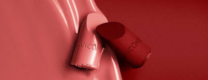A close-up image featuring two lipsticks, one light pink and one deep red, against a smooth, red background. The lipsticks are partially unwrapped, displaying their sleek designs with the brand name "Lancome" visible on the casing.