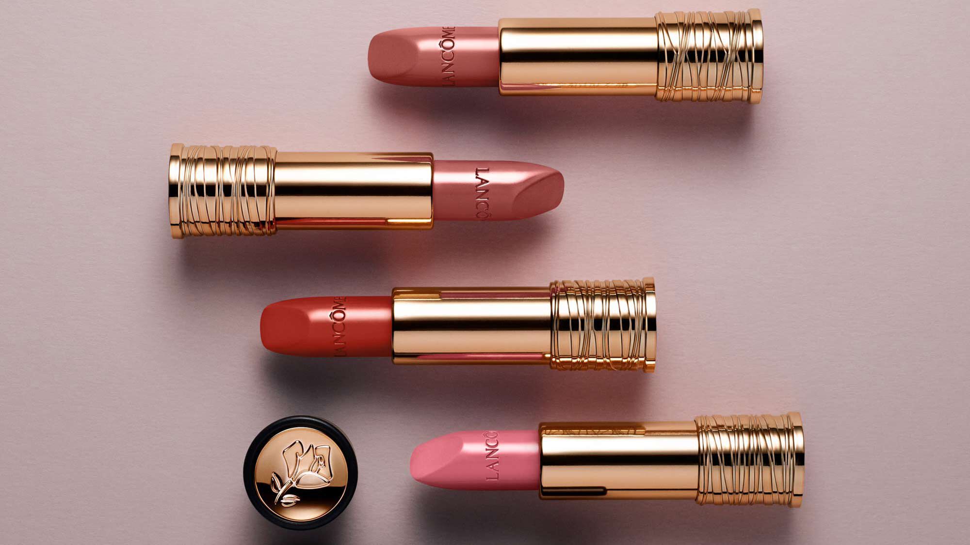A collection of four luxurious lipsticks with gold tubes, featuring shades of pink and coral, arranged neatly on a soft, neutral background.