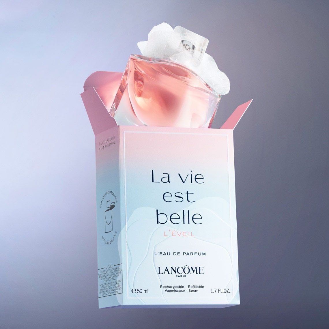 A bottle of Lancome's "La vie est belle L'eveil" perfume, featuring a soft pink liquid and a decorative cap, emerging from its pastel-colored box against a gradient background.