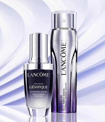 Two Lancome skincare serums are displayed against a soft, wavy background. The products are elegantly arranged, showcasing their sleek packaging.