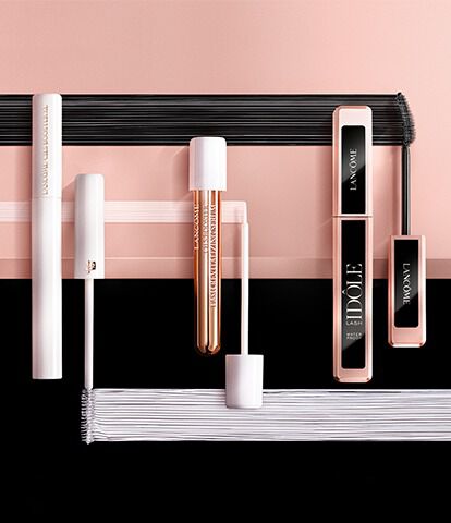 A flat lay arrangement of various beauty products, including lip glosses and mascara, set against a contrasting pink and black background.