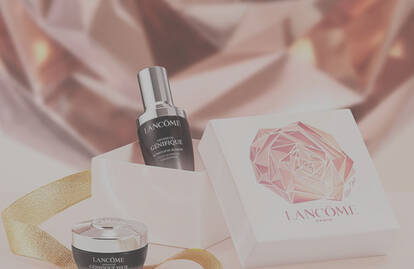 A stylish gift box featuring two Lancome skincare products: a serum and a cream, set against a sparkling, abstract background. There is a gold ribbon adorning the scene.