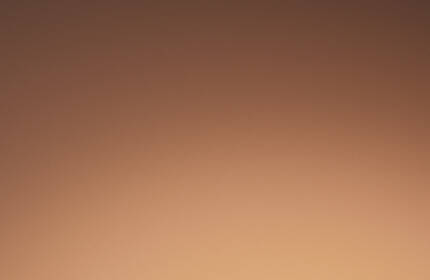 Three bottles of foundation with sleek black caps standing against a warm, gradient background. The labels read "24-Hour Extra Wear."