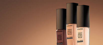 Three bottles of foundation are displayed against a warm, gradient background. Each bottle has a sleek black cap and features labels indicating the product name, "Extreme Wear."