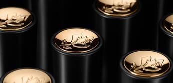 Close-up image of black cylindrical tubes with gold floral logo caps arranged in a visually appealing pattern.