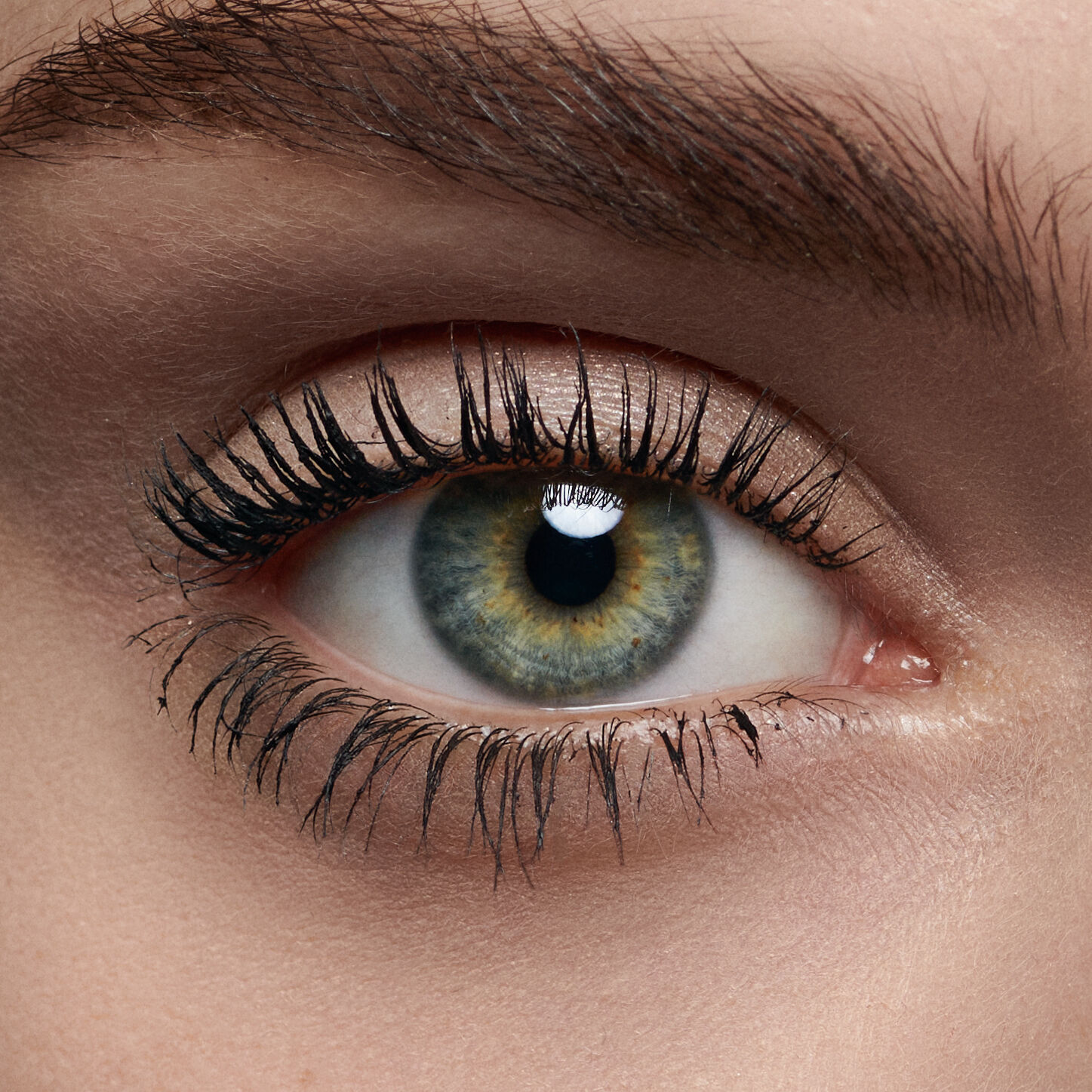 A close-up of a human eye, showcasing a vibrant green and brown iris, along with long, dark eyelashes and smooth skin around the eye.