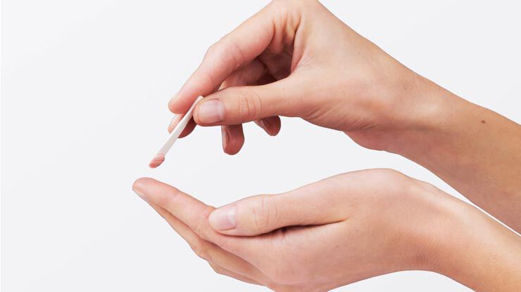 A person is holding a small spatula over one hand, preparing to transfer a small amount of product or cream from the spatula to their palm.