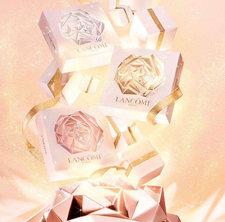 A visually appealing arrangement of elegantly designed Lancome gift boxes in shades of white and rose gold, embellished with shiny gold ribbons, set against a soft pink sparkling background.