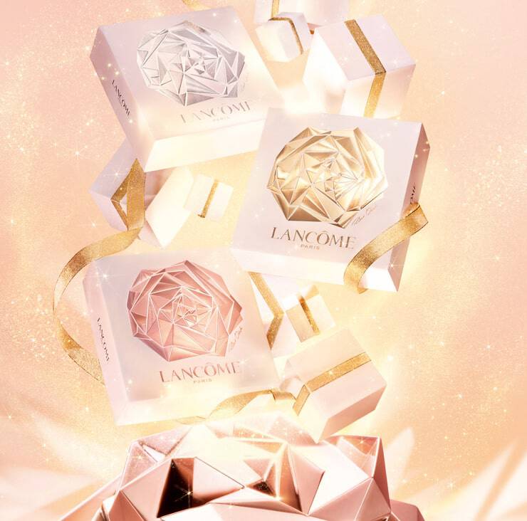 A visually appealing arrangement of elegantly designed Lancome gift boxes in shades of white and rose gold, embellished with shiny gold ribbons, set against a soft pink sparkling background.