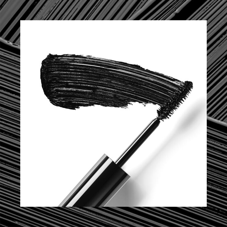 A close-up of a mascara wand with a bold black smear of mascara on a white background.