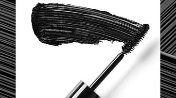 A close-up of a mascara wand with a bold black smear of mascara on a white background.