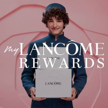 A smiling man in a blue bellhop uniform holds two white Lancome rewards boxes, with the text "my LANCOME REWARDS" overlaid on the image.