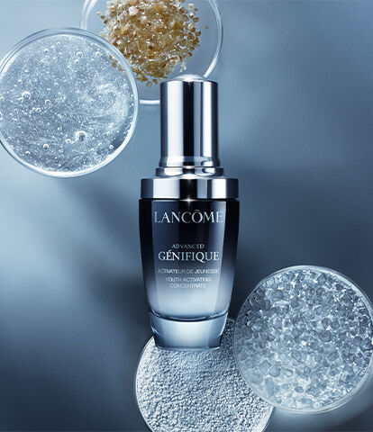 A bottle of Lancome Advanced Genifique serum surrounded by droplets and bubbles, set against a soft blue background.
