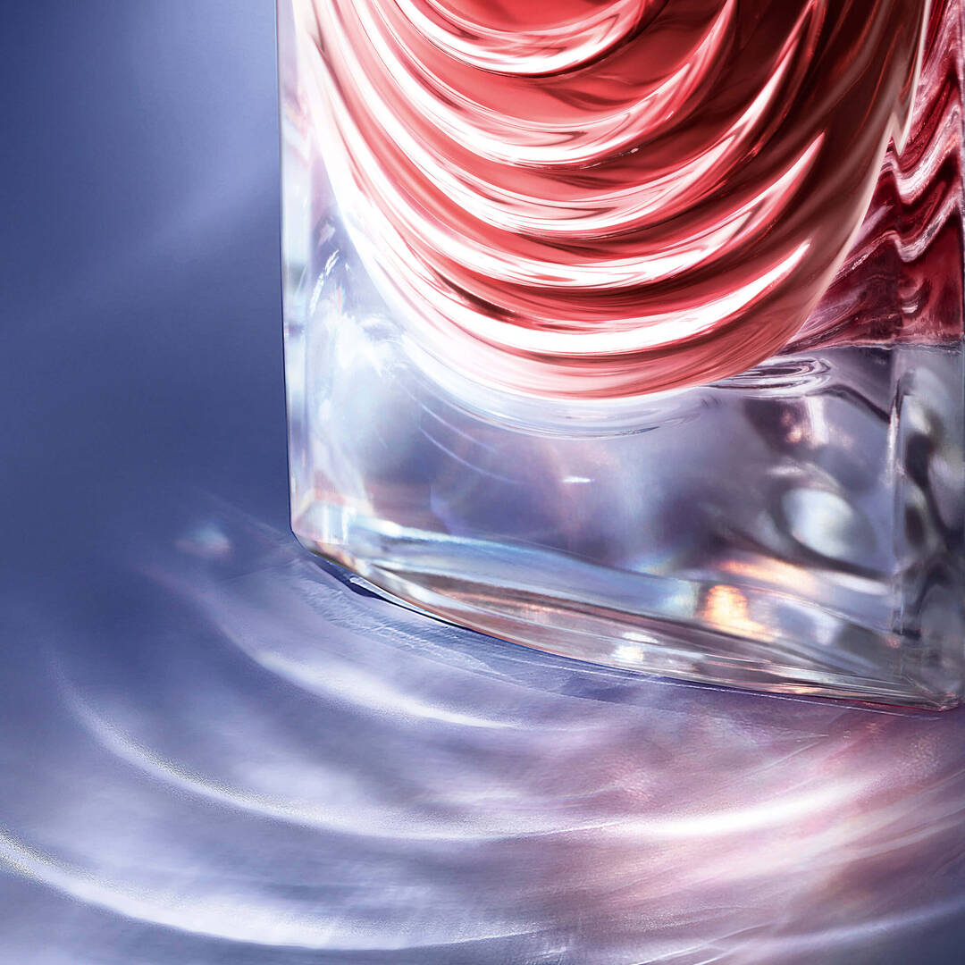A close-up of a glass bottle with a swirling design, reflecting light on a smooth surface, creating colorful patterns in the background.