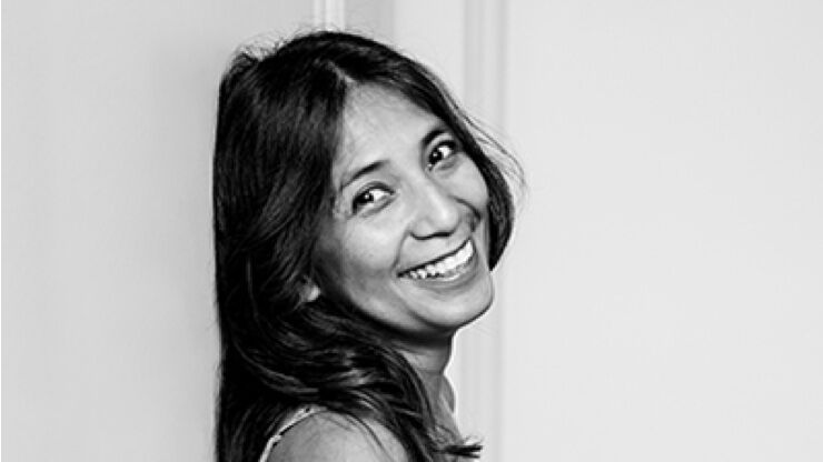 A smiling woman with long, dark hair turns her head towards the camera, creating a warm and inviting expression against a simple background.