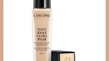 A bottle of Lancome Teint Idole Ultra Wear foundation, featuring a beige liquid formula and a sleek black and gold cap, displayed next to its box.