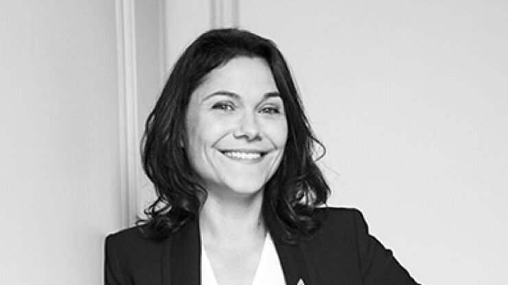 A smiling woman with shoulder-length dark hair, wearing a blazer, stands against a plain background.