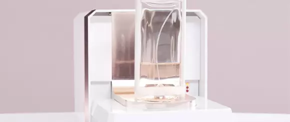 A sleek, modern device with a glass container positioned above a base, featuring a soft gray background.