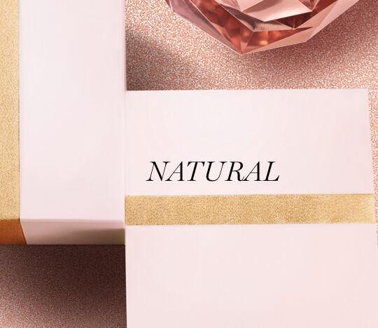 A close-up of two elegantly wrapped boxes with a minimalist design, one featuring the word "NATURAL" in bold black letters, against a sparkling pastel background with a decorative crystal.