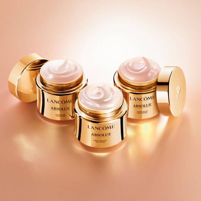 Three jars of Lancome Absolue skincare cream are displayed on a softly lit surface, with golden packaging highlighting the luxurious product.