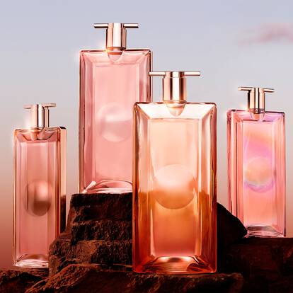 A group of elegantly designed pink glass perfume bottles of varying heights, arranged on a rocky surface against a soft gradient background transitioning from peach to pale pink.