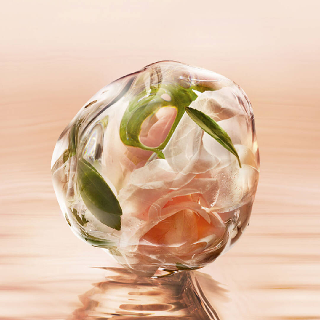 A clear resin orb encasing delicate pink roses and green leaves, reflecting soft light against a peachy background.