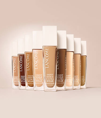 A collection of Lancome foundation bottles arranged in a gradient, showcasing various skin tone shades against a neutral background.