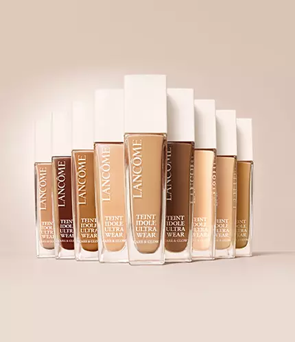 A collection of Lancome foundation bottles arranged in a gradient, showcasing various skin tone shades against a neutral background.
