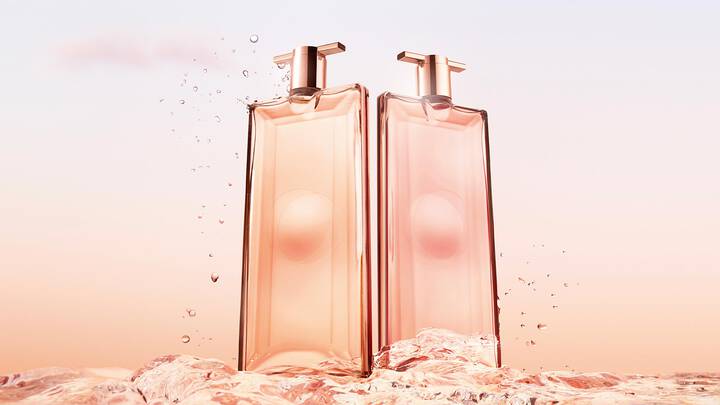 Two elegant fragrance bottles stand against a soft pastel background, partially submerged in water.