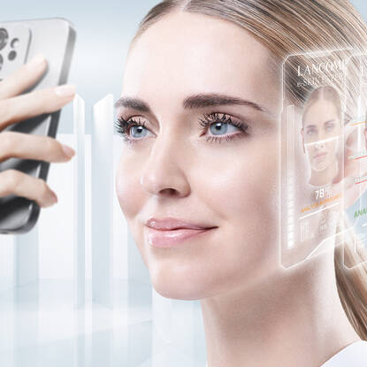 A woman is having her skin analyzed with a digital device, displaying holographic information about skincare products and treatments.