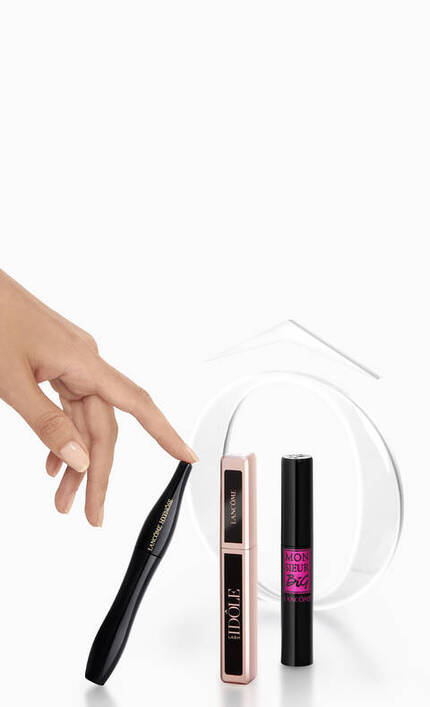 Three mascara tubes in a minimalist setting, with a hand pointing towards the center tube. The background is white.