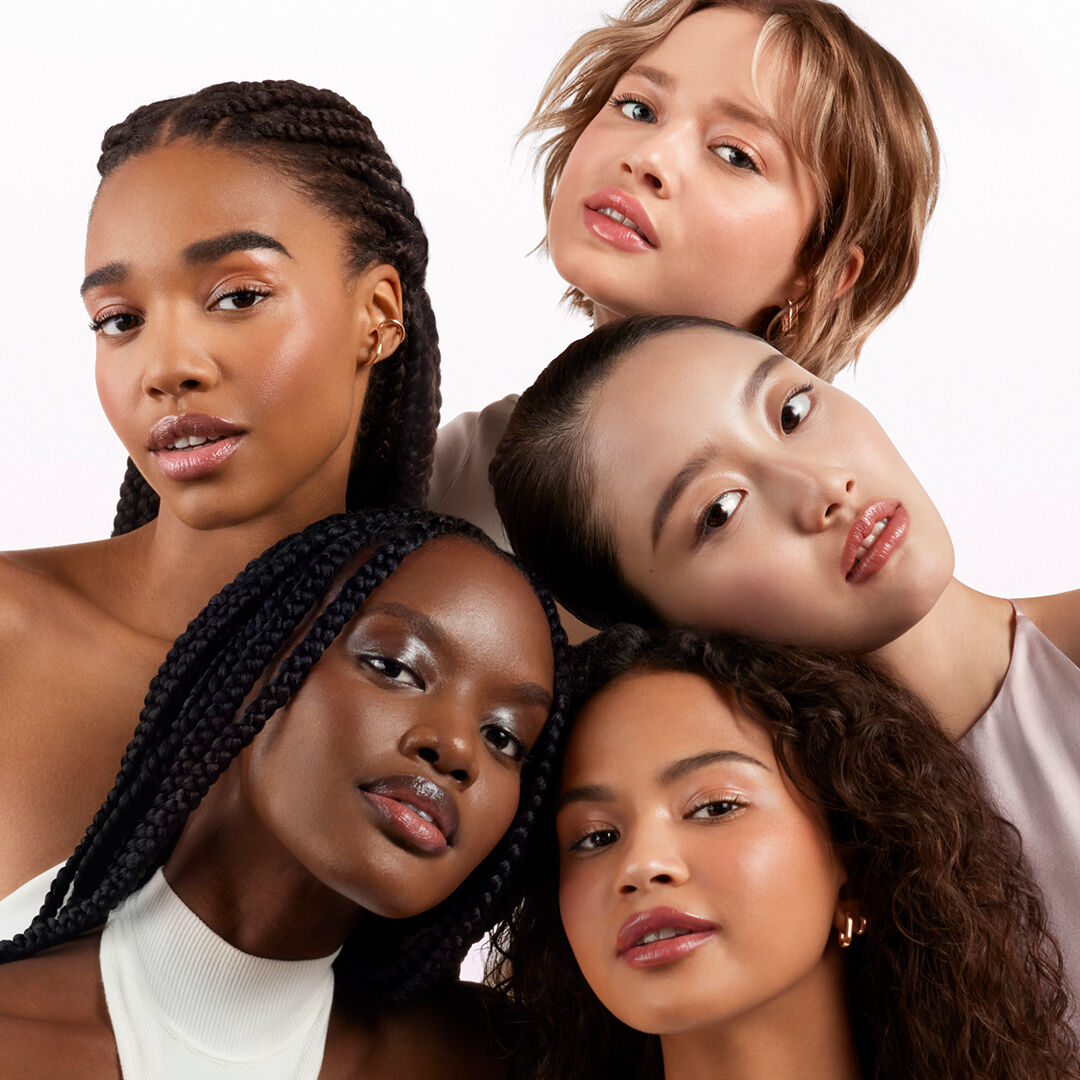 A group of five women of different ethnicities poses closely together, showcasing diverse hairstyles and expressions against a white background.