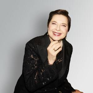 A smiling woman in a black jacket poses against a subtle gray background, showcasing a confident and cheerful demeanor.