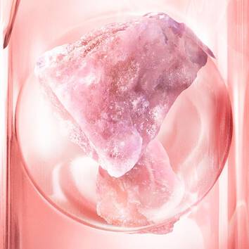 A large pink crystal sits in a circular glass container, reflecting light with a smooth, translucent surface.