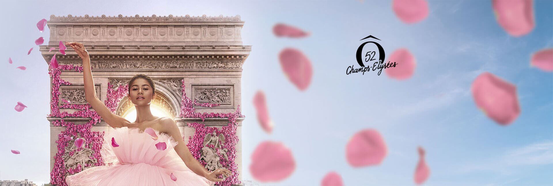 A dancer in a pink tulle dress poses gracefully in front of the Arc de Triomphe, surrounded by floating pink petals. A logo is featured on the right side.