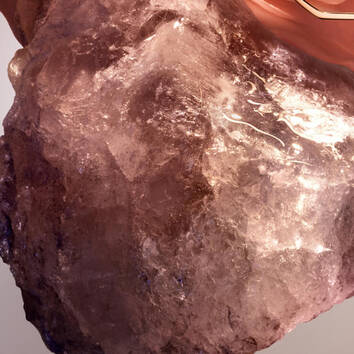 A close-up of a translucent, shimmering quartz crystal with shades of pink and brown, showcasing its natural textures.