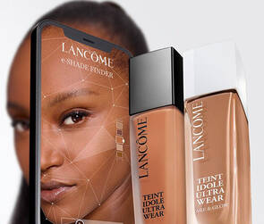 A close-up image showcasing Lancome's Teint Idole Ultra Wear foundation bottles alongside a smartphone displaying a model's face, highlighting the product's beauty features.