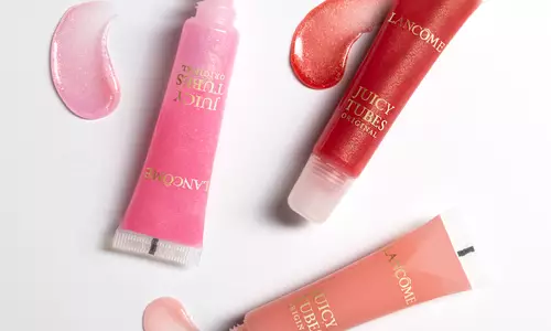 Three tubes of Lancome Juicy Tubes lip gloss in pink, red, and peach shades, with corresponding swirls of gloss beside them.